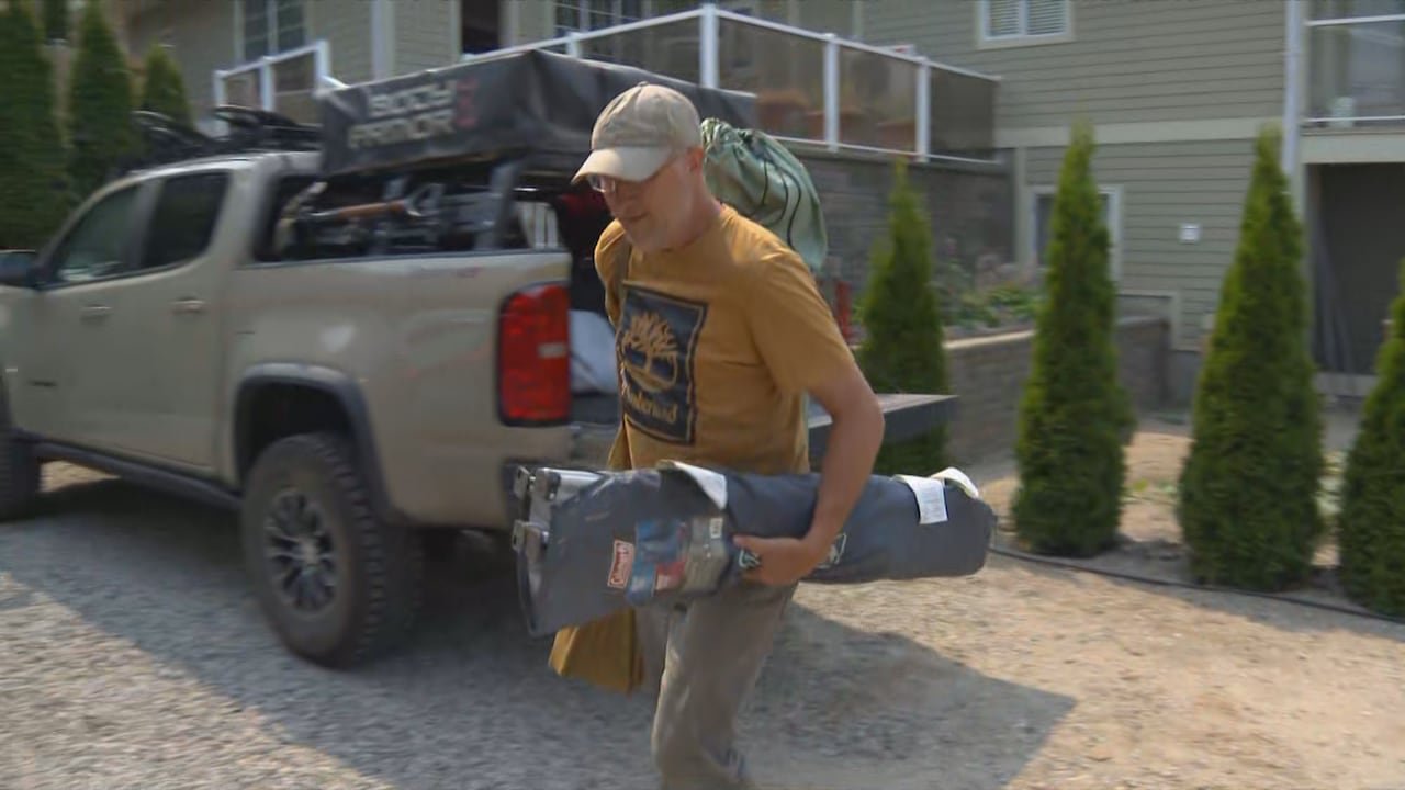 A man holds equipment as he heads into a home next to cars.