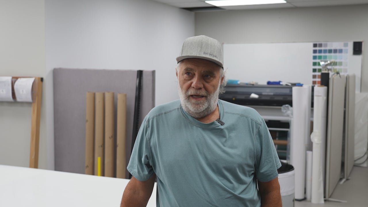 default-1191 A man with a beard and a baseball cap with rolls of wallpaper in the background.