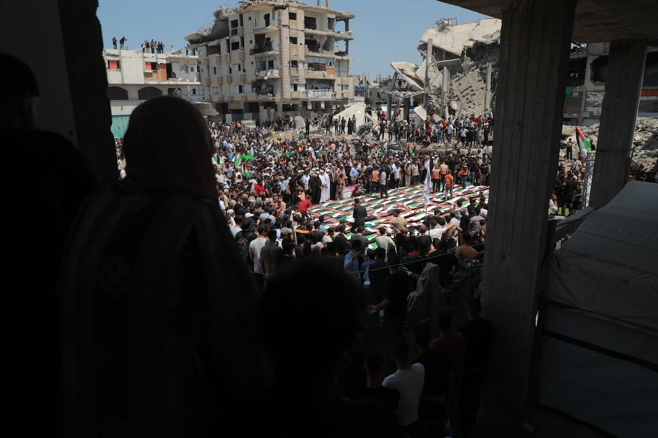 People look out from a building as mourners gather around funeral shrouds made from Palestinian flags.