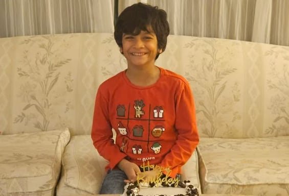 A young boy smiling behind a birthday cake.