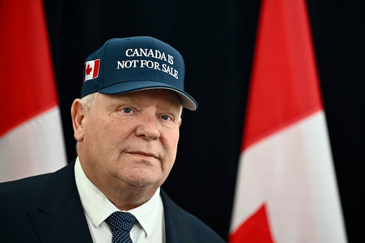 Man wearing dark blue hat with a Canadian flag on the side and the words "Canada Is Not For Sale" on the front in white text
