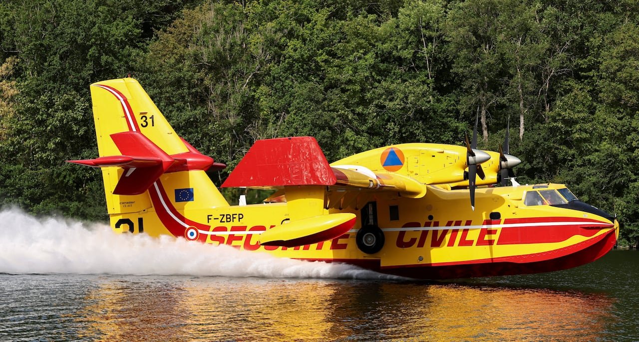 The yellow and red aircraft scoops up water while flying over the river.