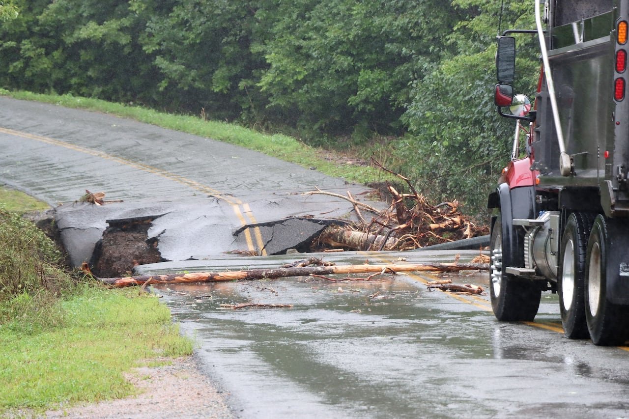 A large truck is stopped just before a break in a paved road, with the asphalt crumbling away.