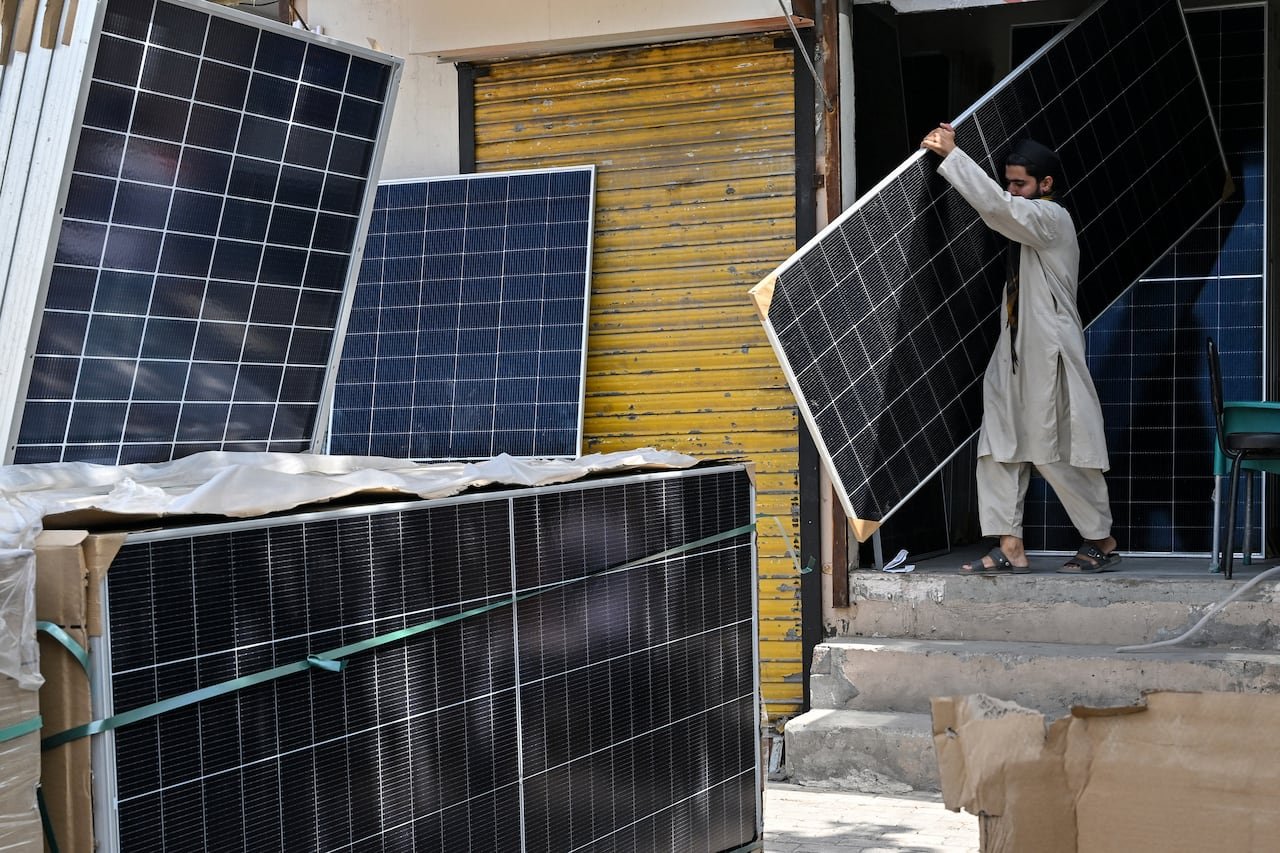 A man carries a large black panel near other panels stacked outside.