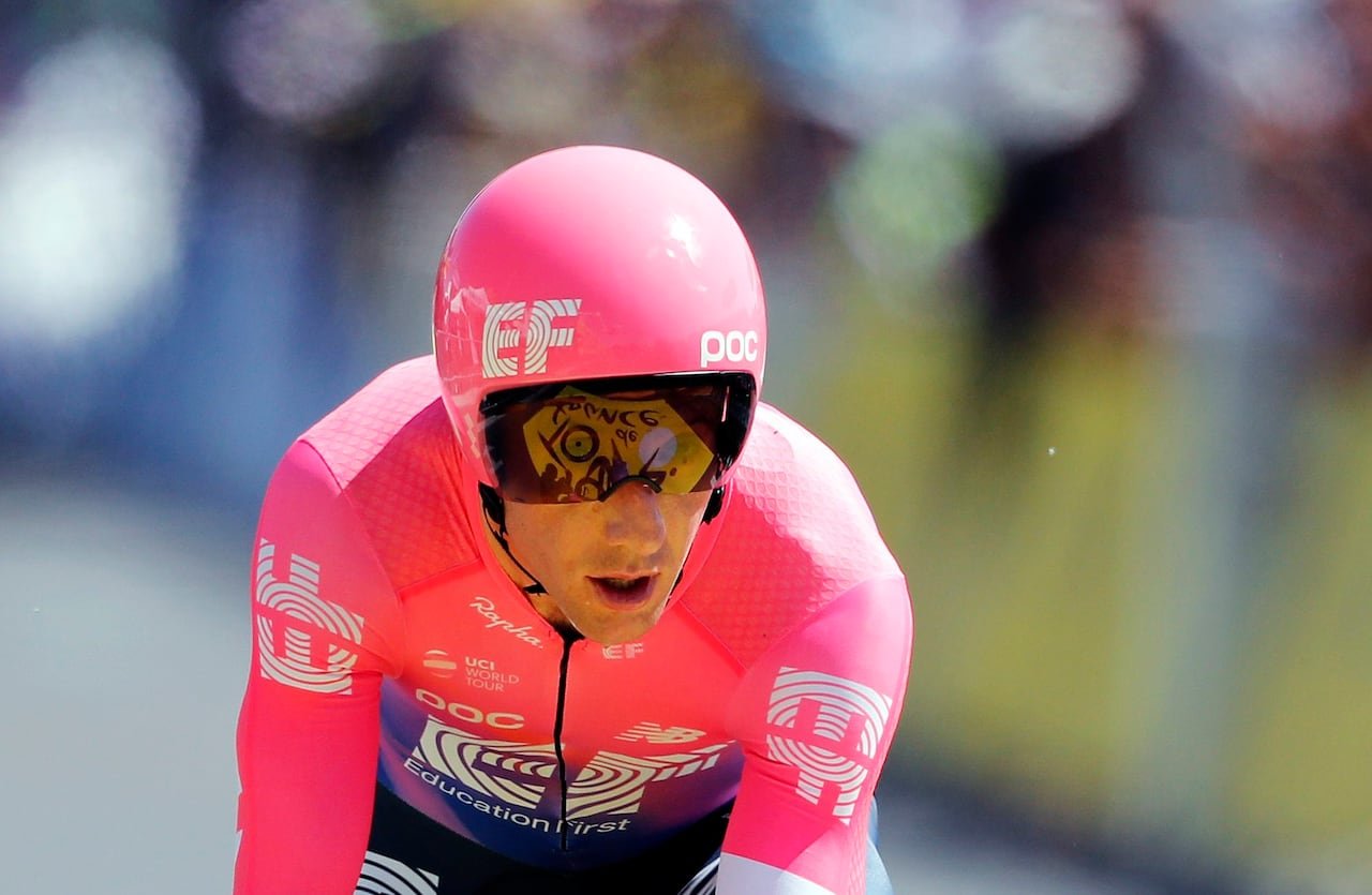 A cyclist in a pink shirt and helmet is leaning over a bike.