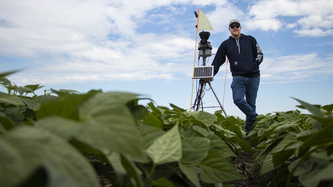 A farmer stands by a weather station in a field.