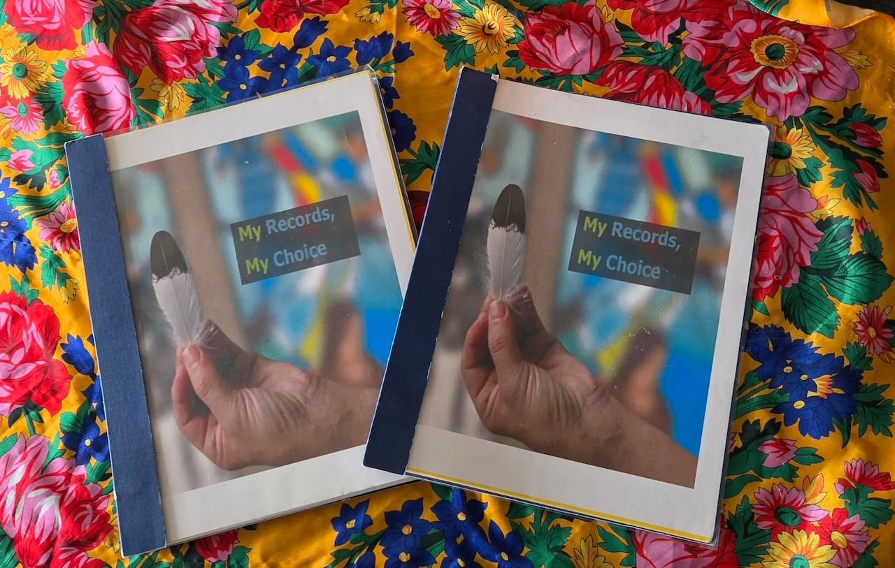 default-2946 Two thick booklets resting on a colorful tablecloth. Both feature an identical cover displaying an image of a hand holding an eagle feather with the words "My Records, My Choice" printed on them.