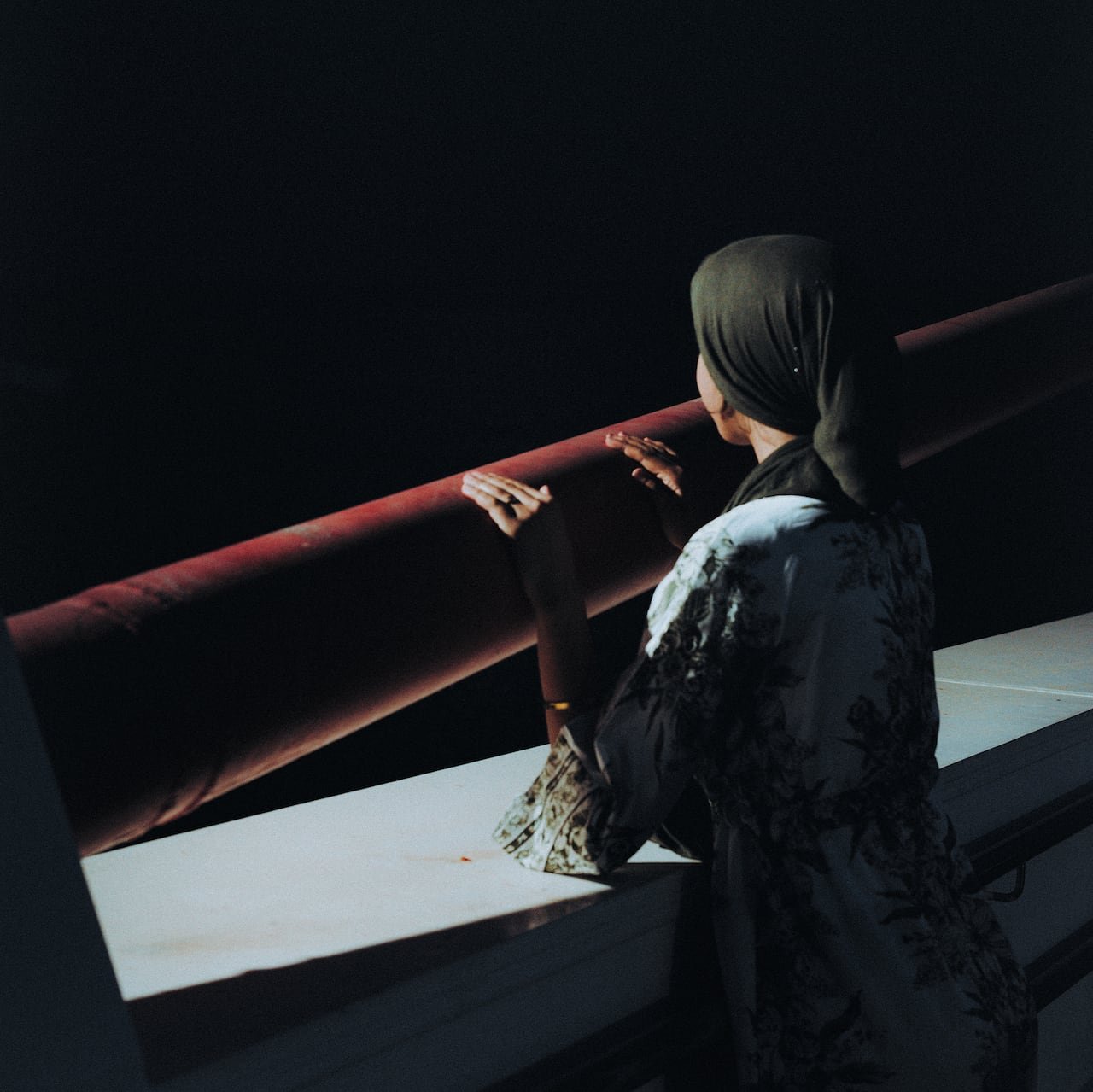 A young woman in a headscarf looks out from a bridge.