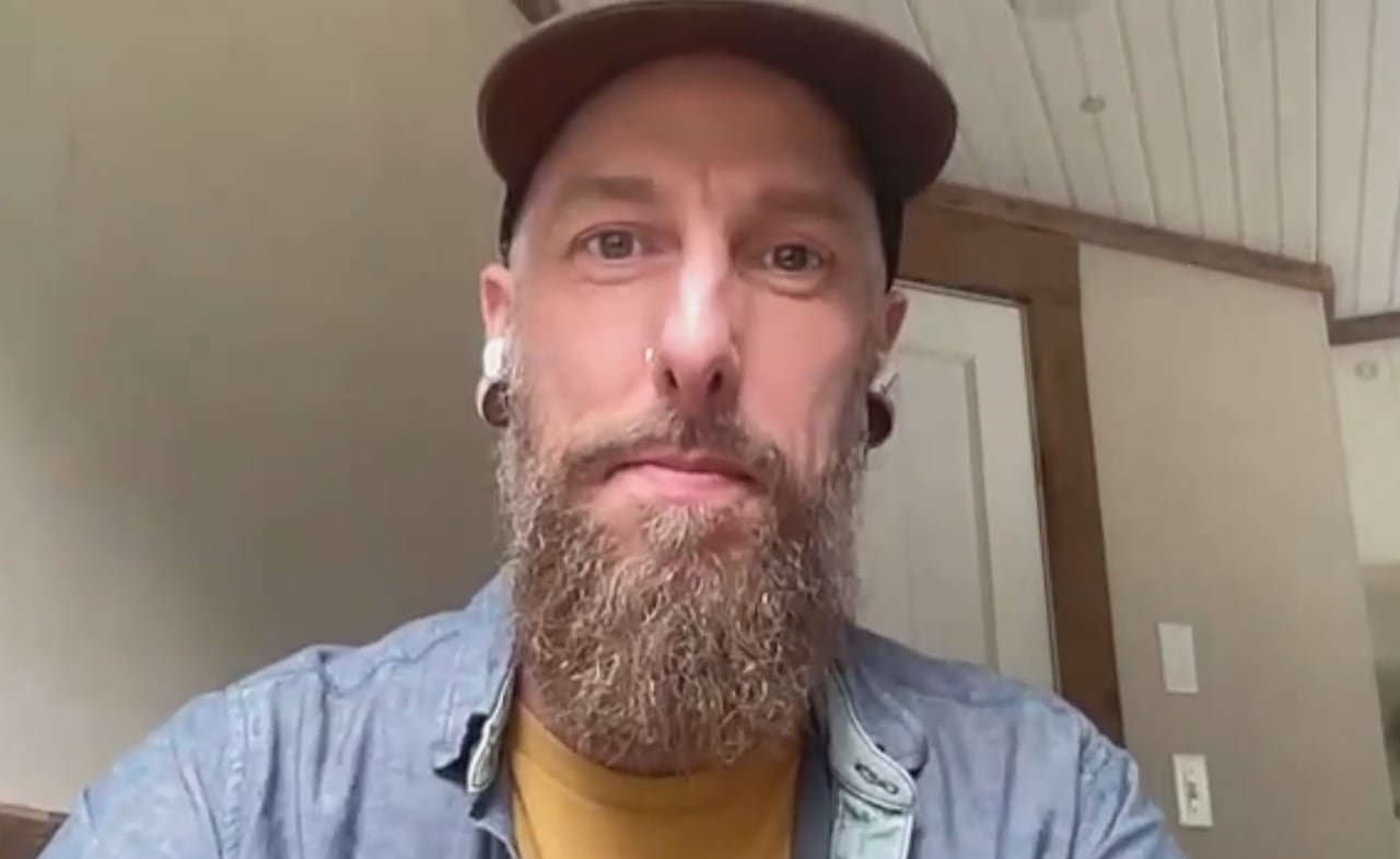 Man with a beard wearing a hat and button-up shirt.