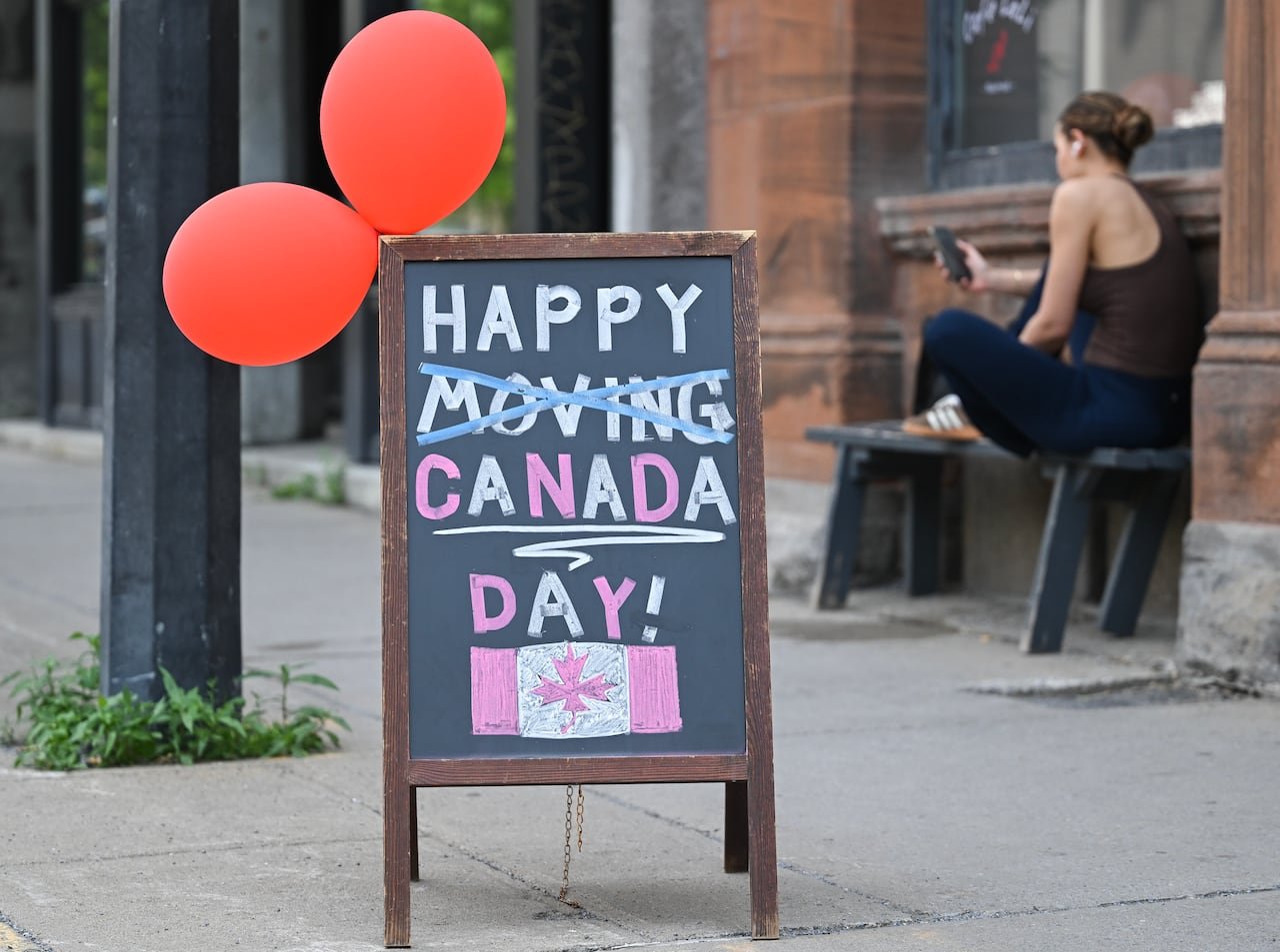 default-1225 A black chalk sign says, "HAPPY CANADA DAY!" The word "moving" has been crossed out.