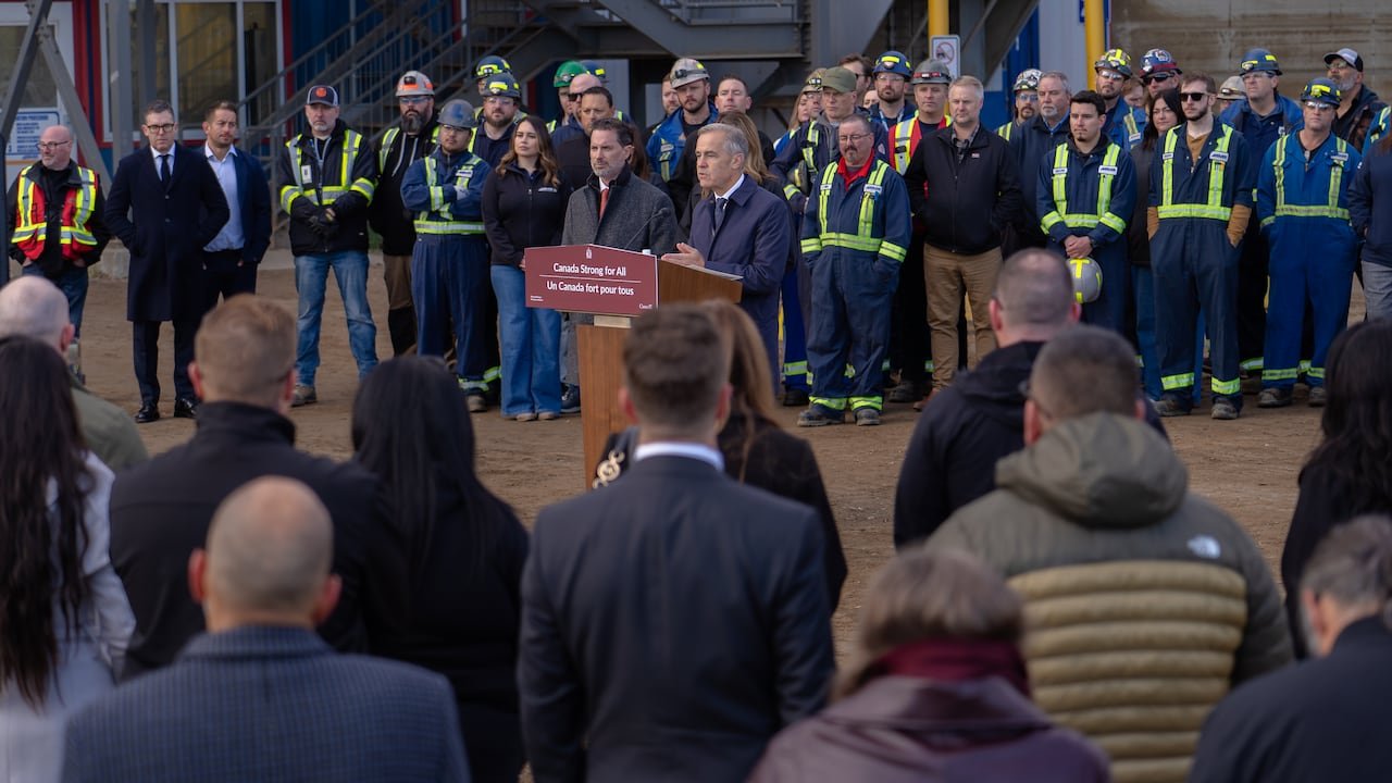 default-2292 A man at a podium speaks to a crowd while workers are in the background.