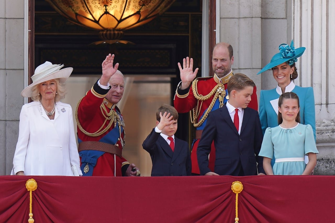 default-474 Four adults and three children wave as they stand on the balcony of a large stone building.